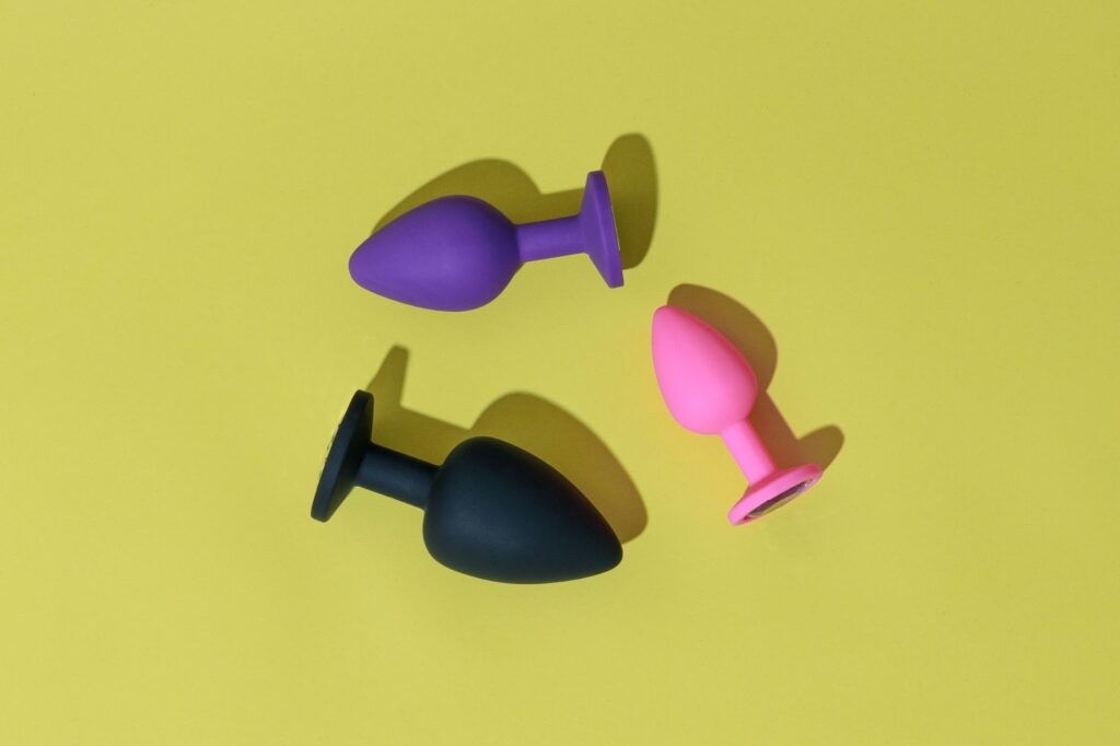 Different coloured adult sex toys butt plugs on a yellow background