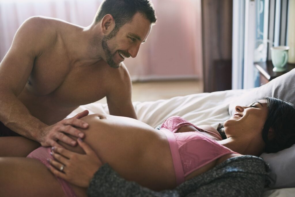 Happy male and pregnant female smiling in bed