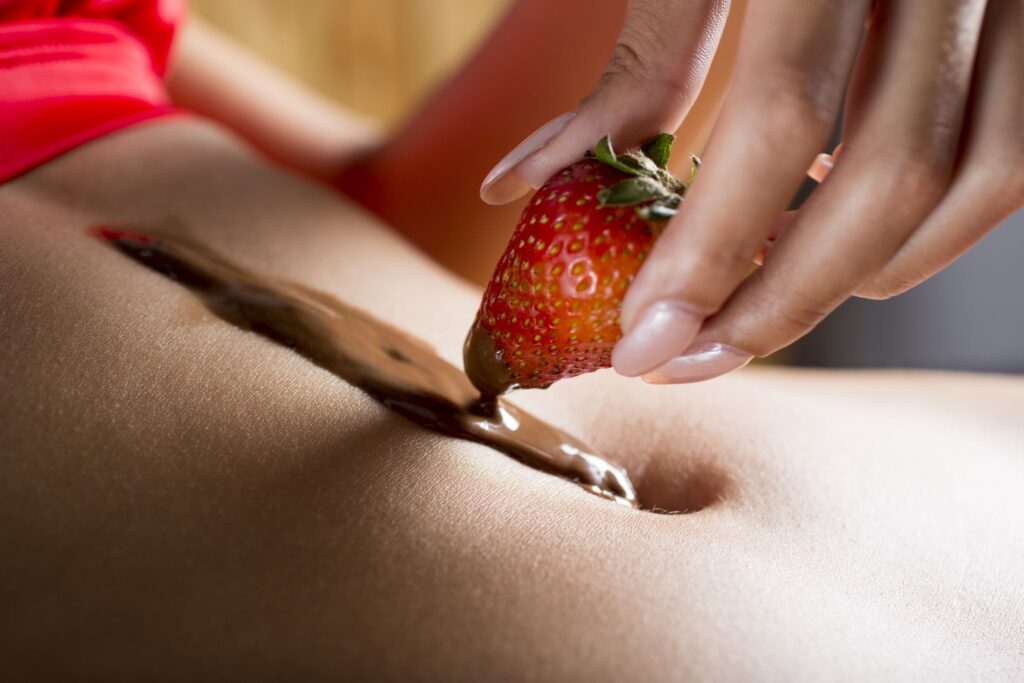A woman's stomach with chocolate sauce and a strawberry.