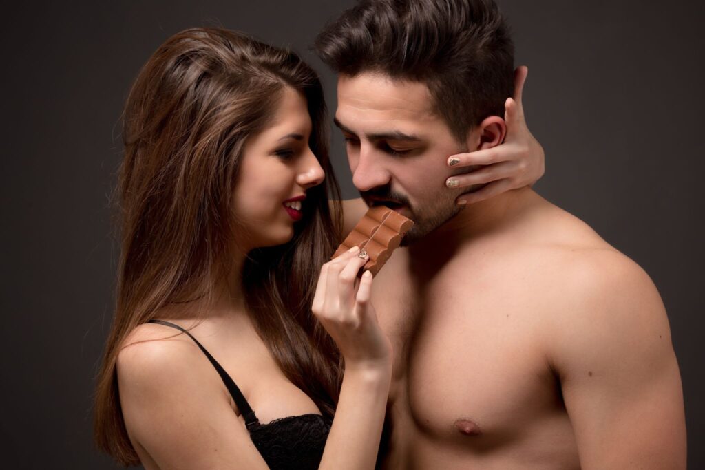 A woman feeding a shirtless man chocolate