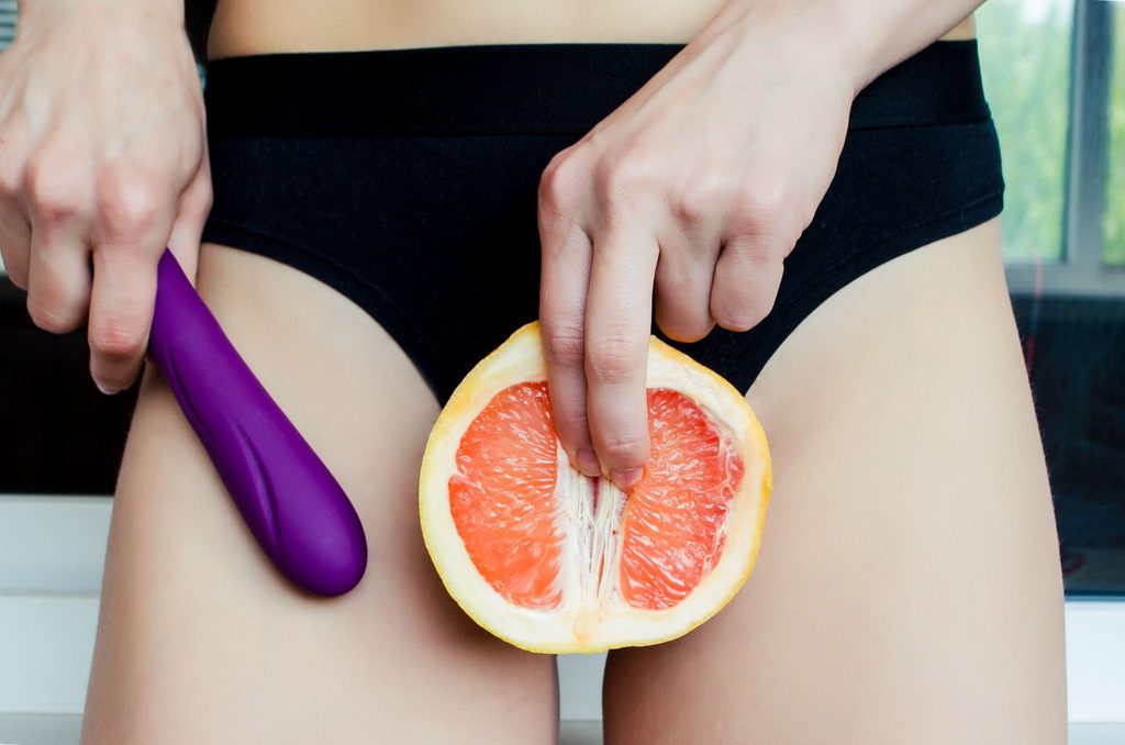 A woman in black underwear holding a grapefruit and a sex toy